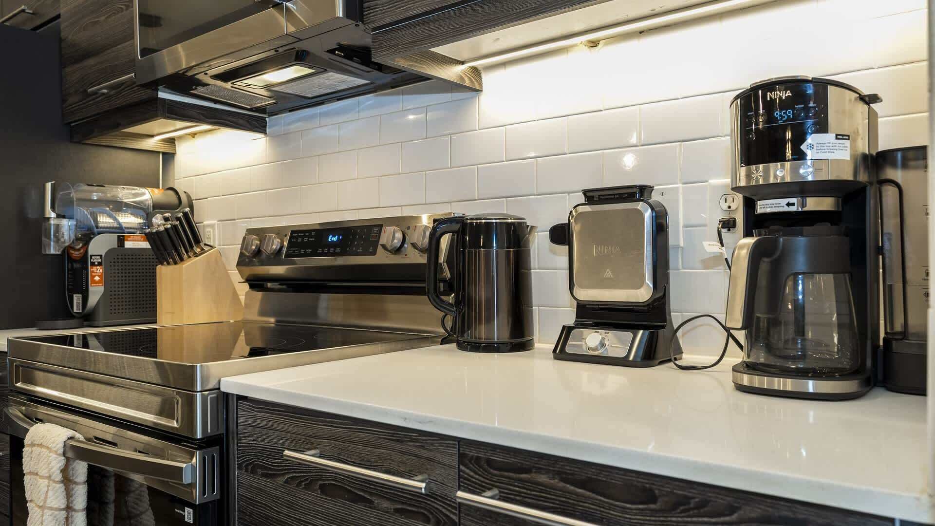 Una cocina moderna con electrodomésticos de acero inoxidable, incluyendo una cafetera, un hervidor y un horno.