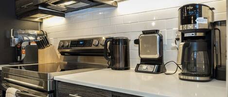Una cocina moderna con electrodomésticos de acero inoxidable, incluyendo una cafetera, un hervidor y un horno.