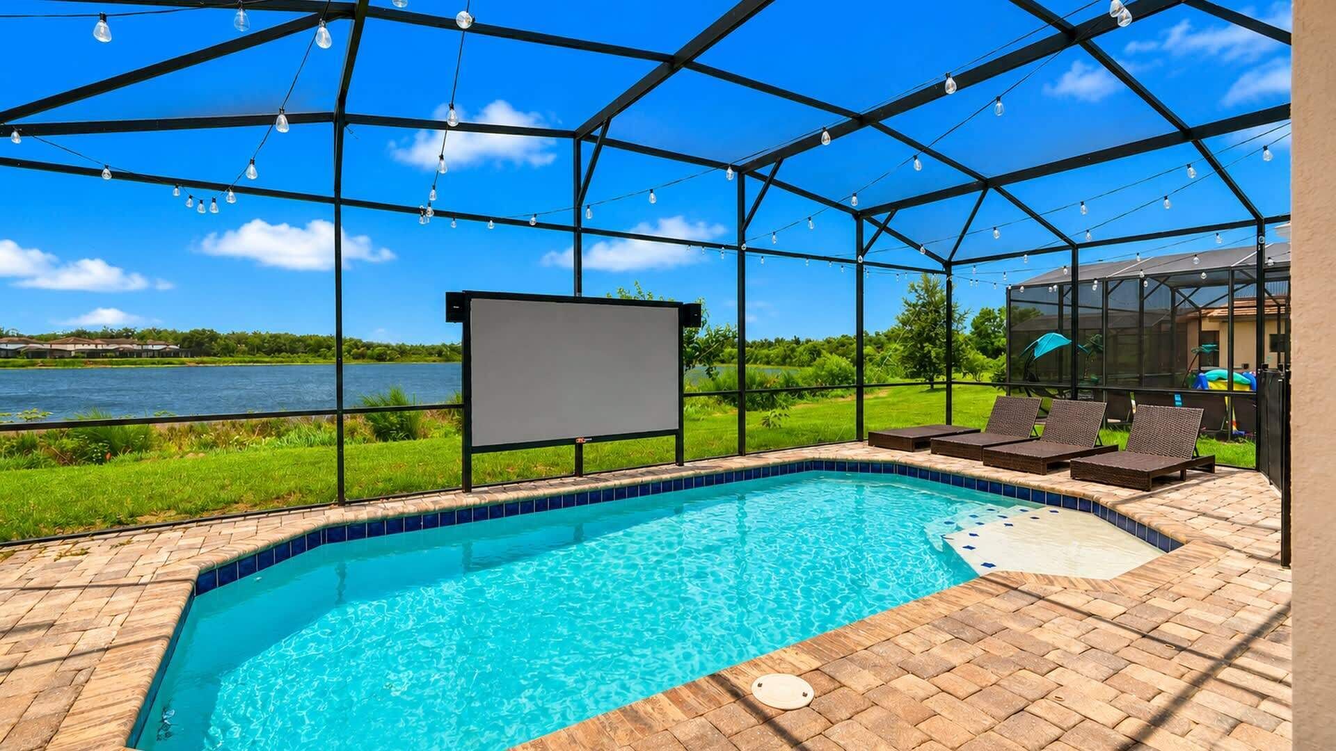 Una piscina con vista despejada a un lago, rodeada por un área techada con asientos y una pantalla para ver al aire libre.