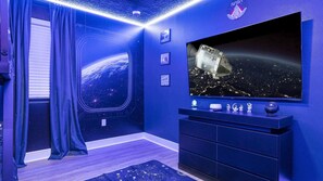 Ein Zimmer mit einem großen Flachbildfernseher, der eine Weltraumansicht zeigt, einem Fenster mit Blick auf die Erde und einem SpaceX-Logo an der Wand.