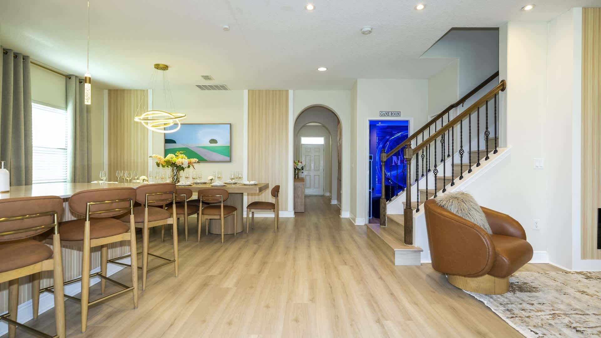 Amplia sala de estar con una mesa de comedor preparada para seis personas, una escalera y un letrero que indica una sala de juegos.