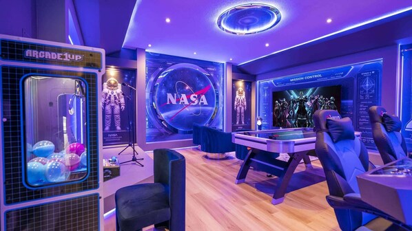 A room with a NASA-themed decor, including a large NASA logo, a space-themed wall, and a gaming area with a pool table and arcade games. - Luxury Villa Pool Lake View at Balmoral Resort (Haines City)