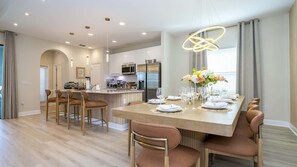 A modern kitchen with stainless steel appliances and a dining area with a wooden table set for a meal. - Luxury Villa Pool Lake View at Balmoral Resort (Haines City)