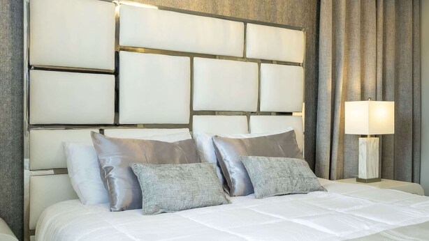 Ett hotellrum med en stor säng, en sänggavel med ett geometriskt mönster och en sänglampa.
