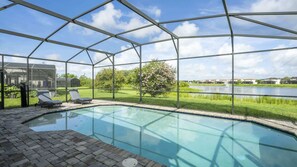 Ein Swimmingpool mit Glasveranda, Liegestühlen und Blick auf einen See sowie Gebäude.