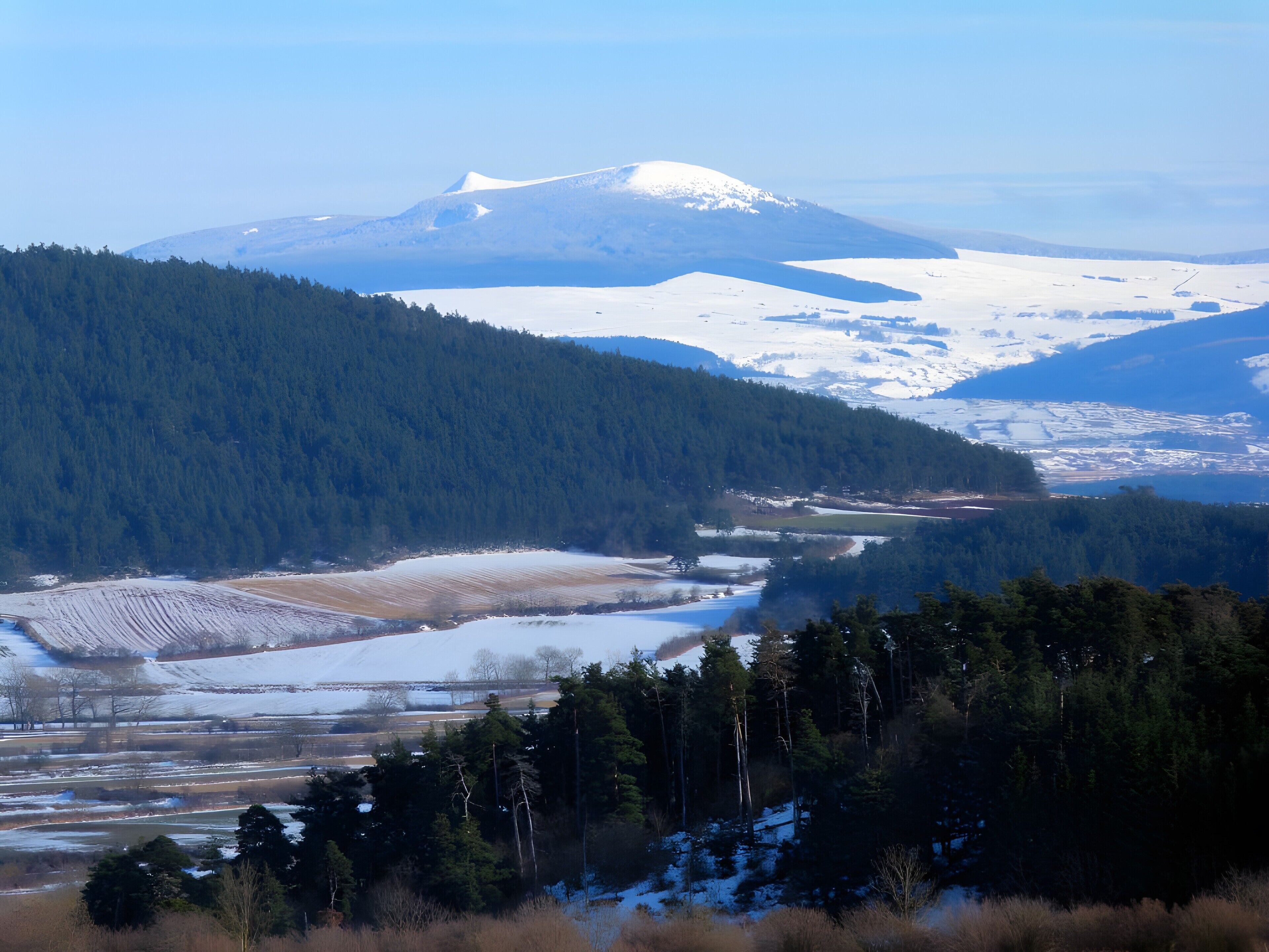 A mountainous landscape with a snow-covered peak, dense forests, and a river.