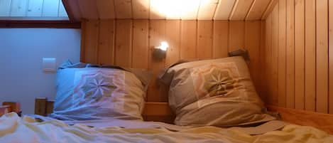 A room with a sloped ceiling and wooden walls, featuring two beds with pillows and a nightstand.