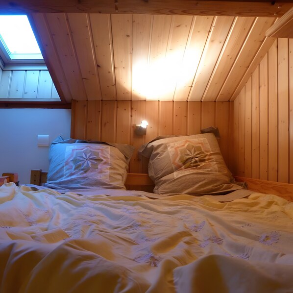A room with a sloped ceiling and wooden walls, featuring two beds with pillows and a nightstand.