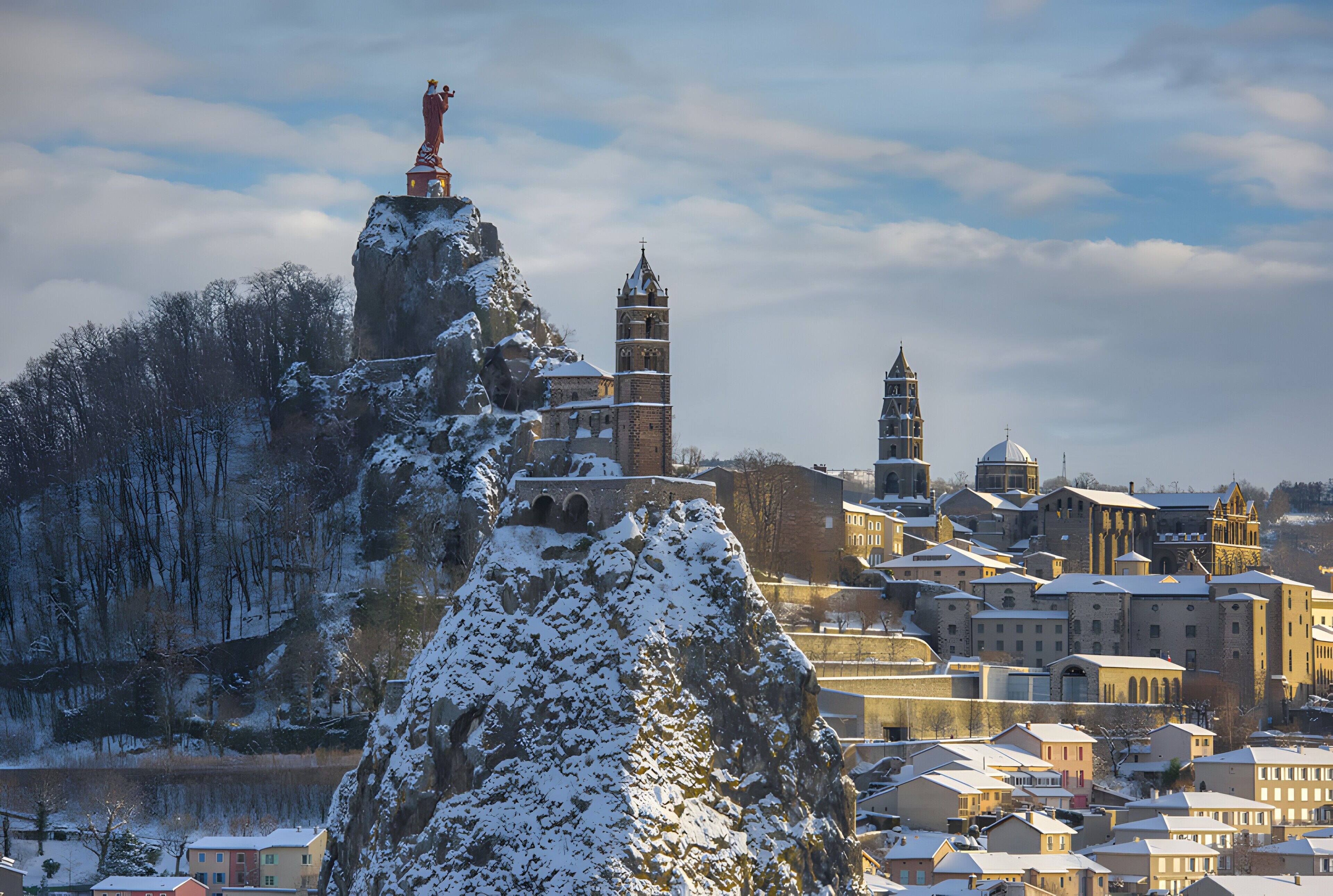 Eine historische Stadt mit einem markanten Kirchturm, einer Statue auf einem Felsen und schneebedeckten Gebäuden.