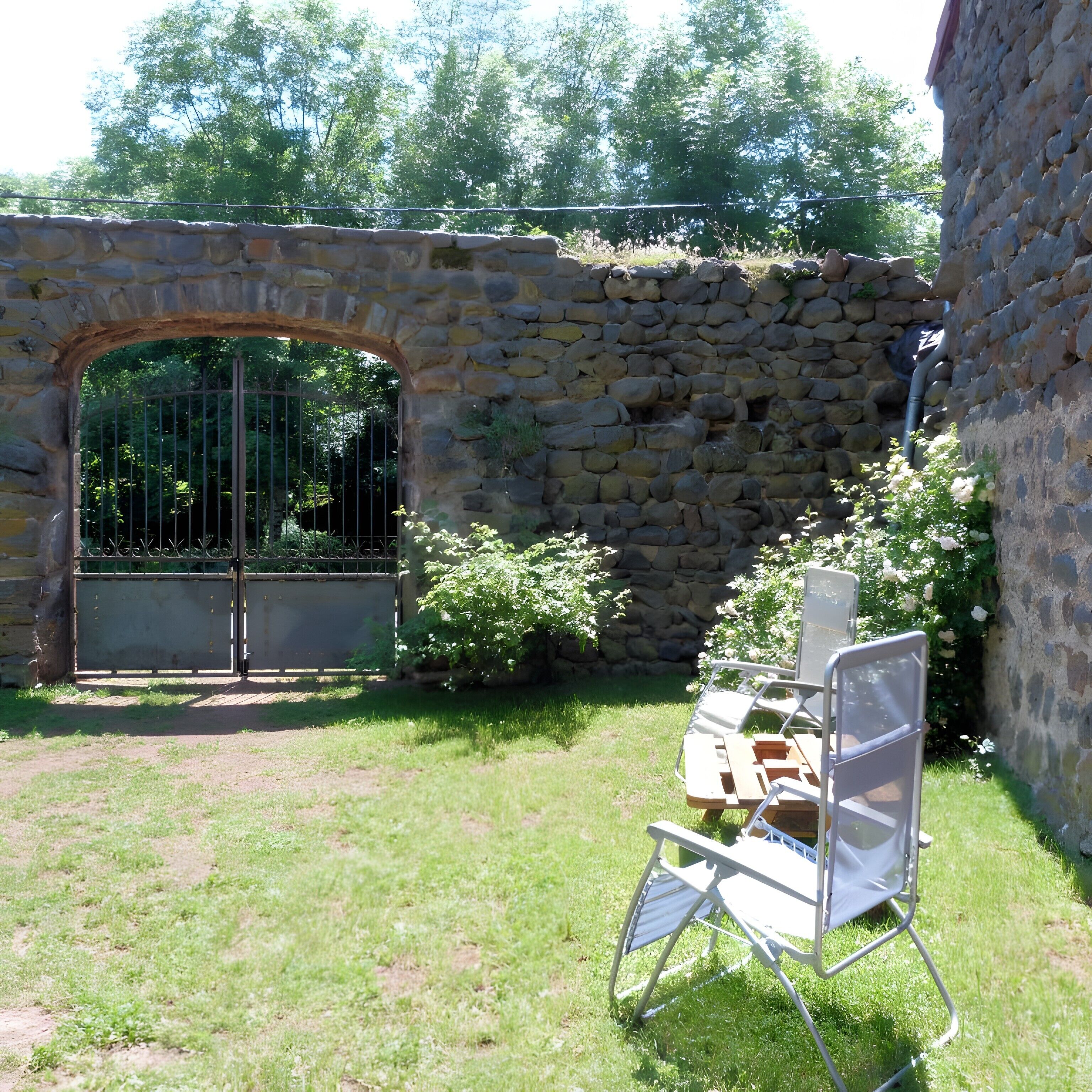 A stone wall with a metal gate, a grassy area, and a metal chair with a table.
