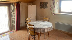 A dining area with a round table, chairs, a refrigerator, and a window with curtains.