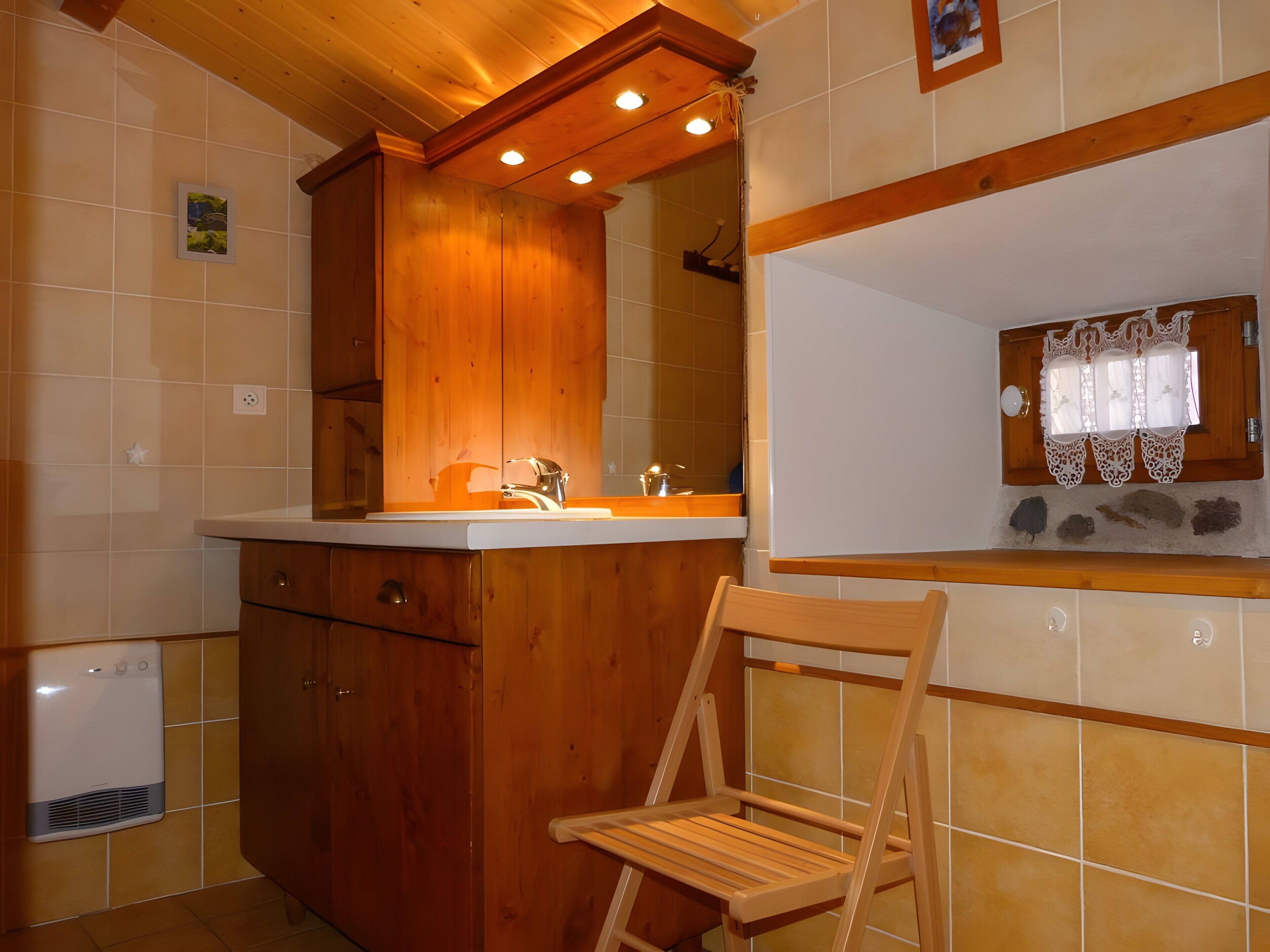Une cuisine avec des meubles de rangement en bois, un évier et une fenêtre ornée de rideaux en dentelle.