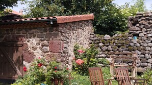A rustic stone wall with a tiled roof, surrounded by lush greenery and flowering plants.