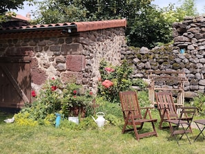 A rustic stone wall with a tiled roof, surrounded by lush greenery and flowering plants.