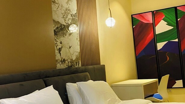 A modern bedroom with a large bed, a headboard, a bedside table, and a wall with a decorative panel.