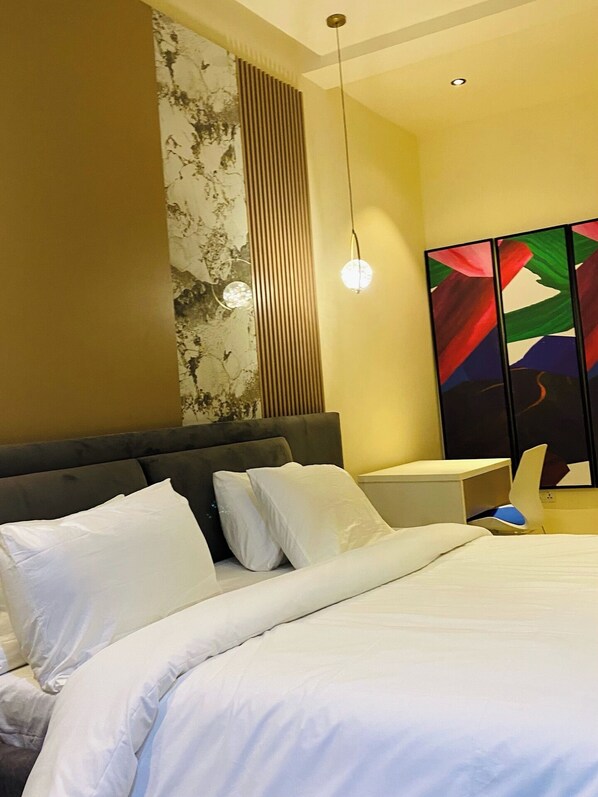 Un dormitorio moderno con una cama grande, cabecera, mesita de noche y una pared con panel decorativo.