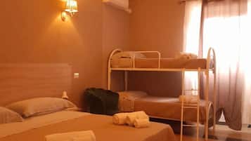A hotel room with two beds, a bunk bed, a wall-mounted air conditioner, and a window with curtains.
