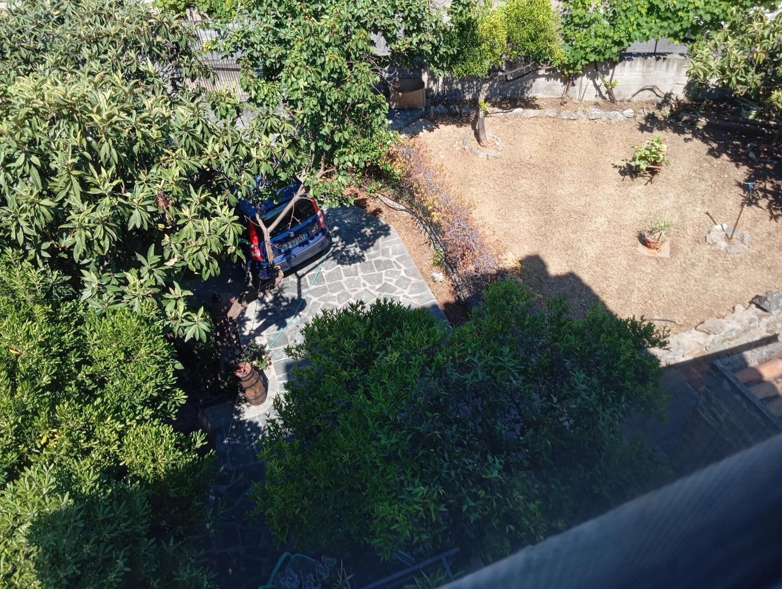 An aerial view of a courtyard with a parked vehicle, a stone pathway, and surrounding greenery.