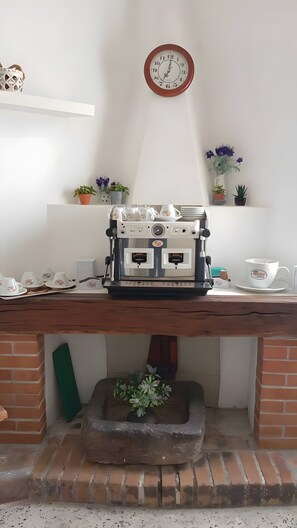 A coffee machine on a wooden table with a clock above it, surrounded by potted plants and cups.