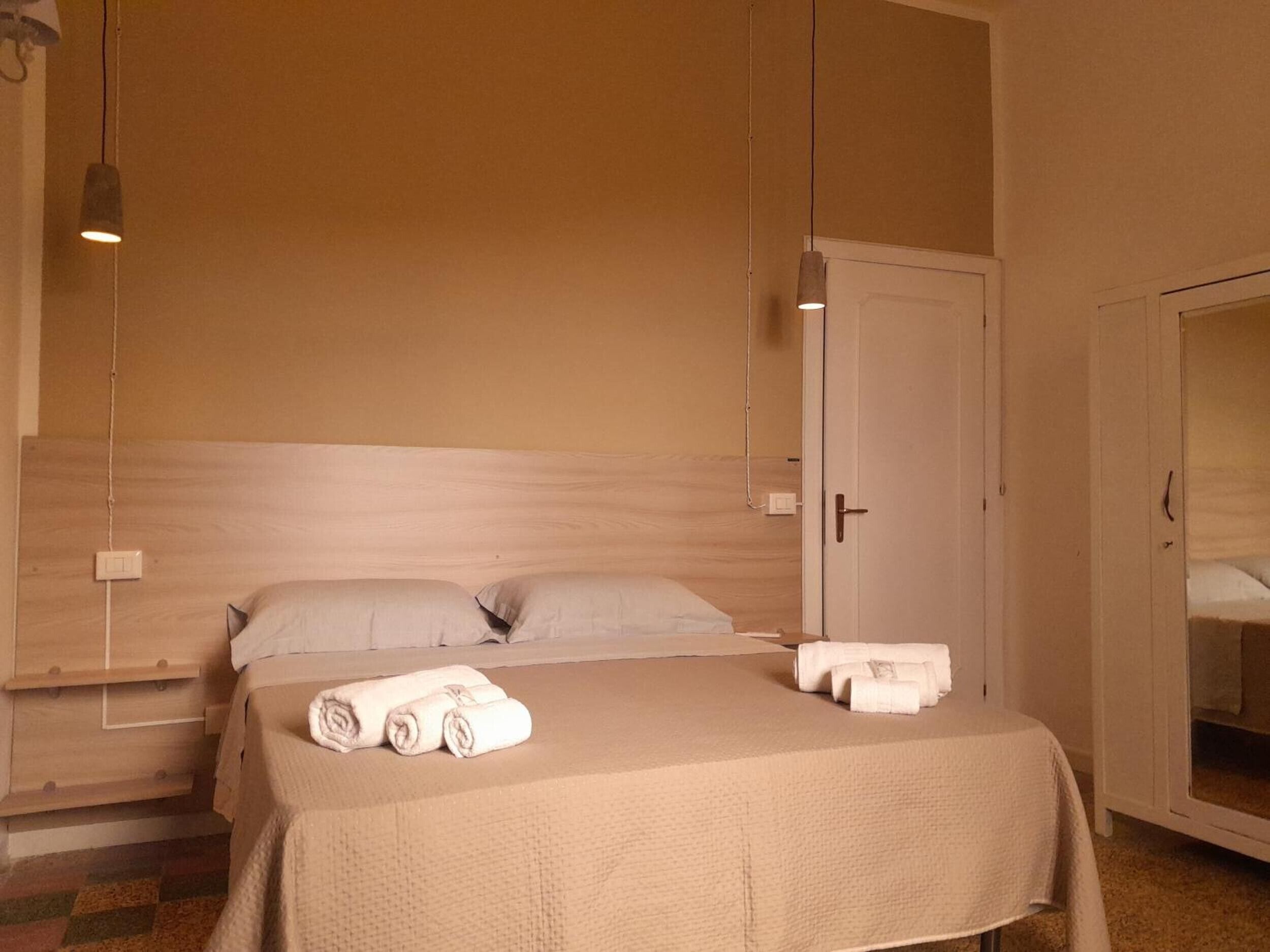 Une chambre d’hôtel avec un lit, deux oreillers, une table de chevet, un miroir et une porte.