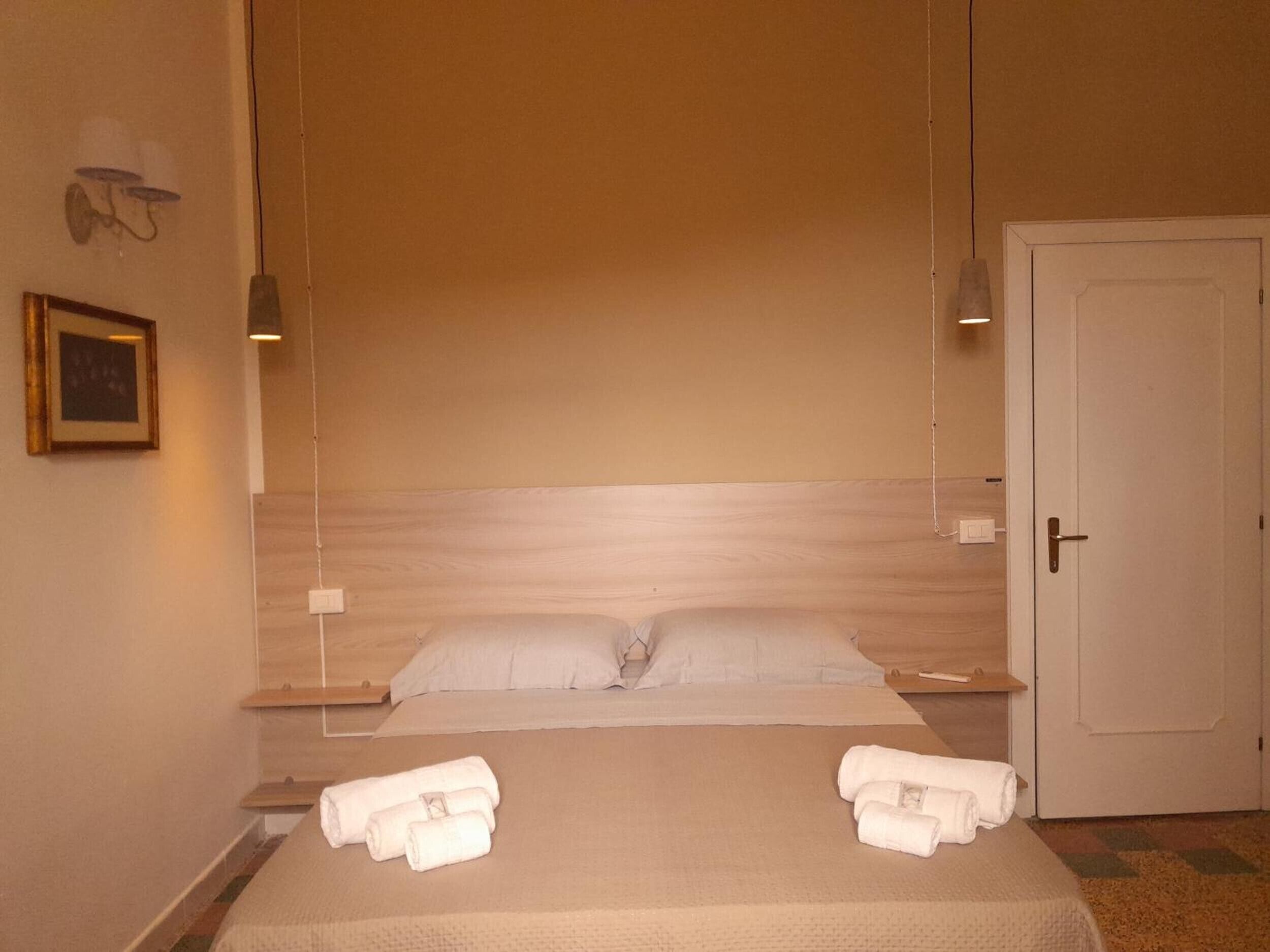 Een hotelkamer met een bed, twee nachtkastjes, een deur en een lampje aan de muur.