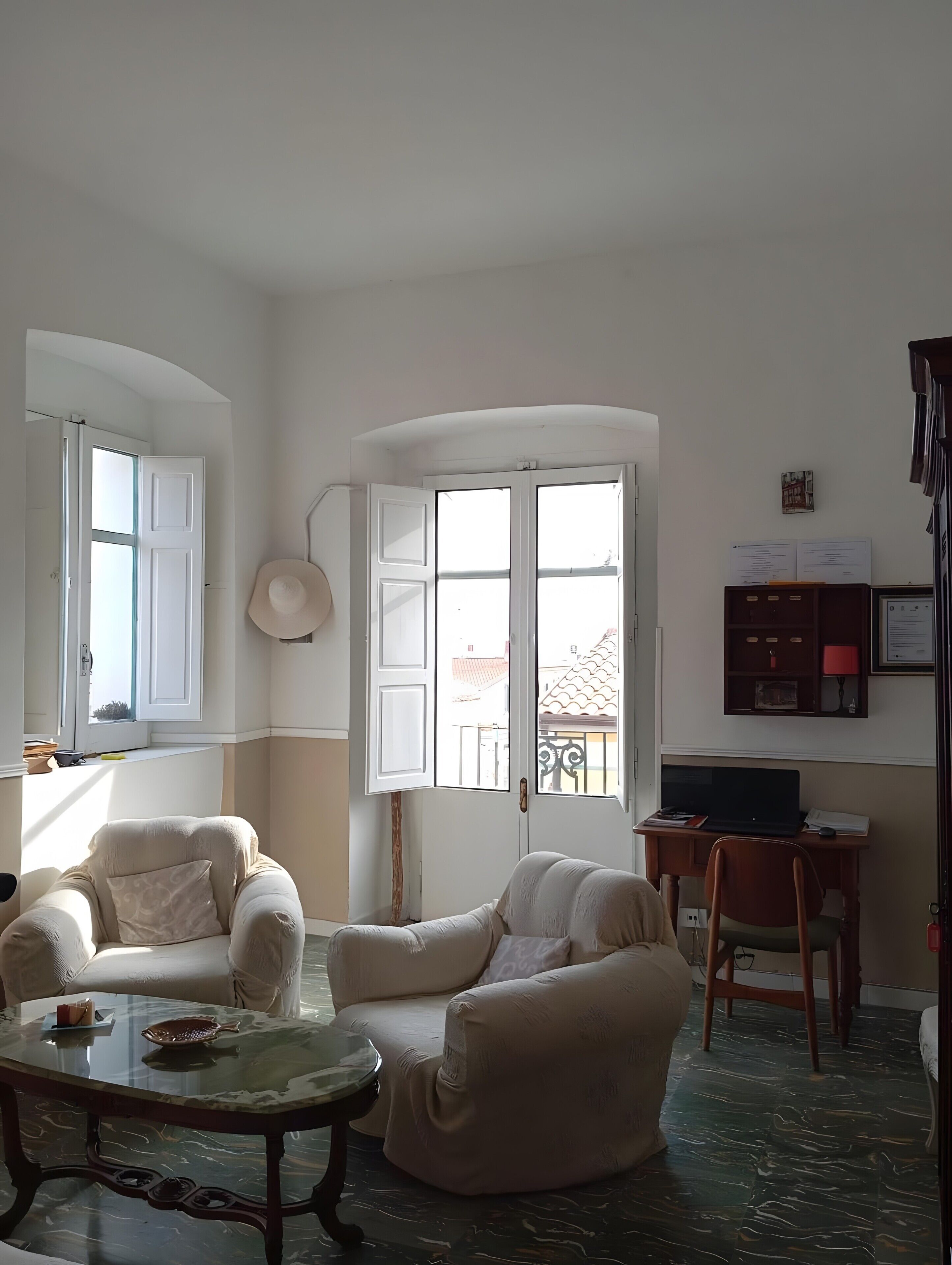 A living room with two sofas, a glass coffee table, a desk with a laptop, and a view through a large window.