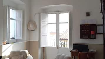 A living room with two sofas, a glass coffee table, a desk with a laptop, and a view through a large window.