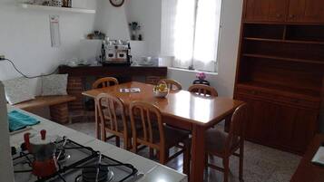 Une cuisine équipée d’une cuisinière à gaz, de chaises en bois, d’une table à manger et d’une fenêtre avec des rideaux.