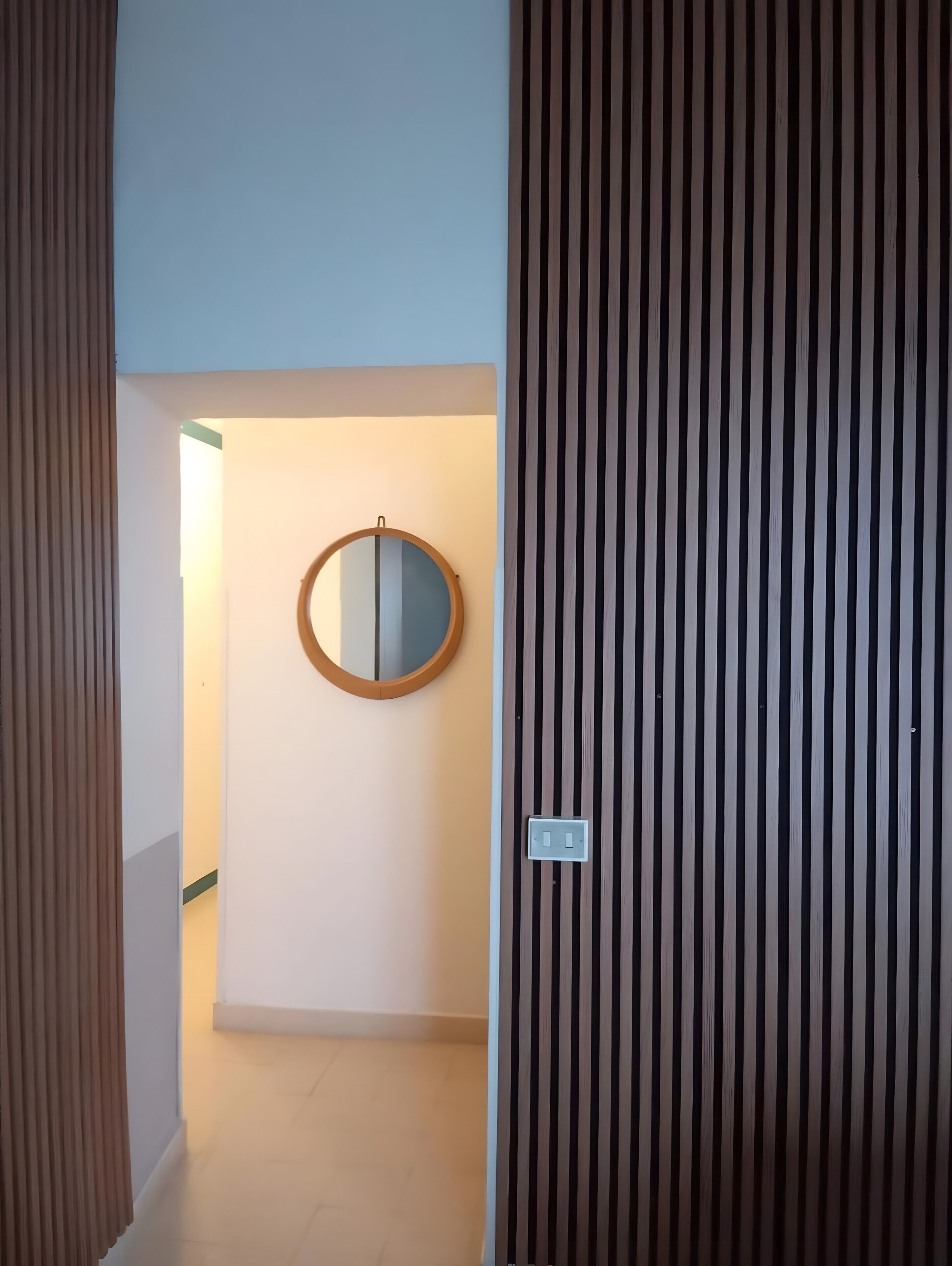 Une pièce avec un miroir encadré en bois accroché au mur, un interrupteur et un rideau à rayures.