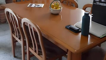 Un coin repas avec une table en bois, des chaises, un saladier de fruits, une bouteille d’eau et une machine à café.