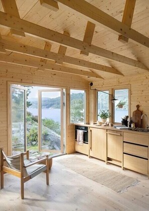 Ein Holzinterieur mit einer Küche, einem Essbereich und großen Fenstern mit Blick ins Freie.