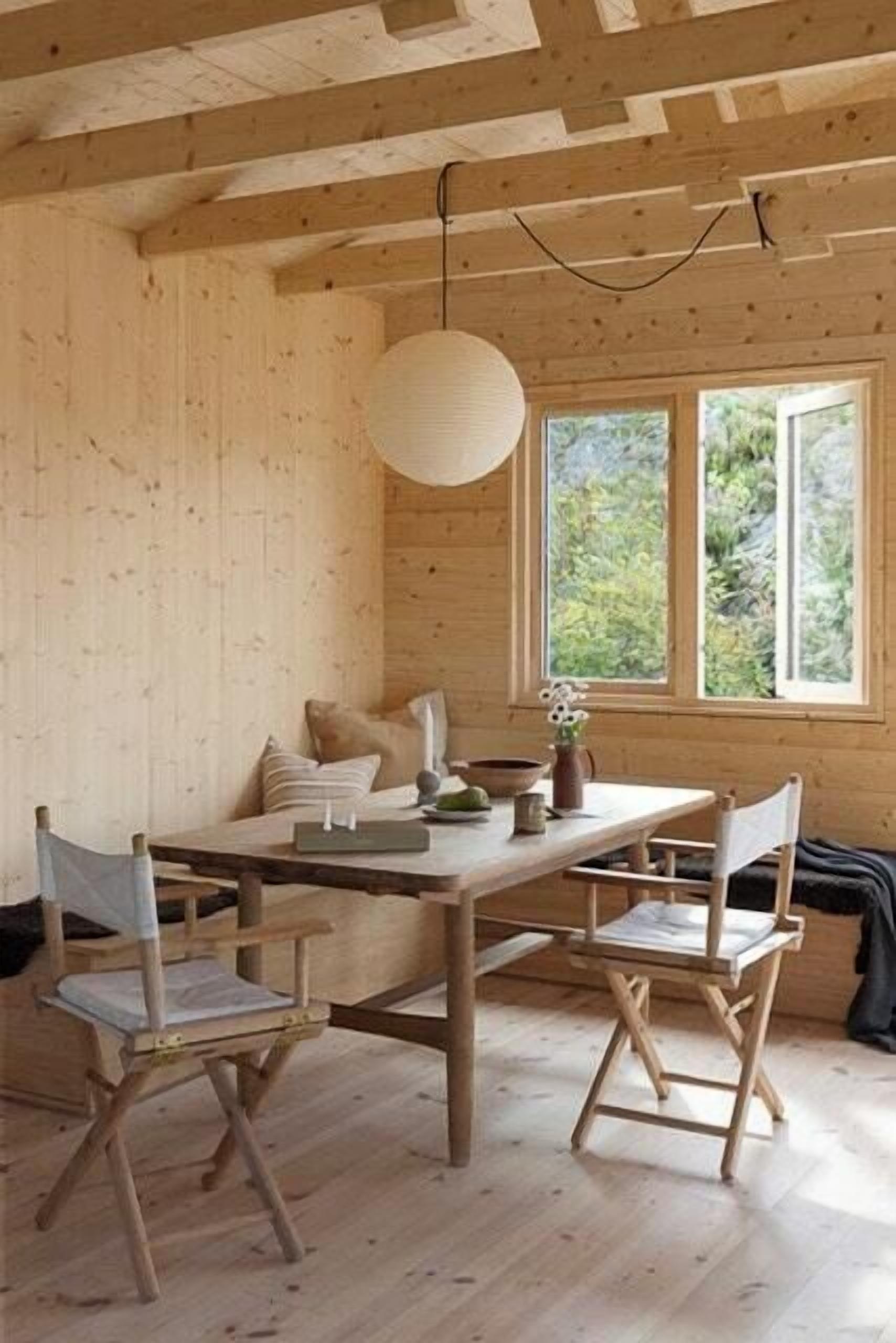 A wooden interior with a dining table, chairs, and a hanging light fixture.
