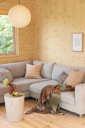 A cozy living room with a sectional sofa, a round wooden side table, and a hanging light fixture. - Cottage gem with views of the Oslo Fjord (Akershus)