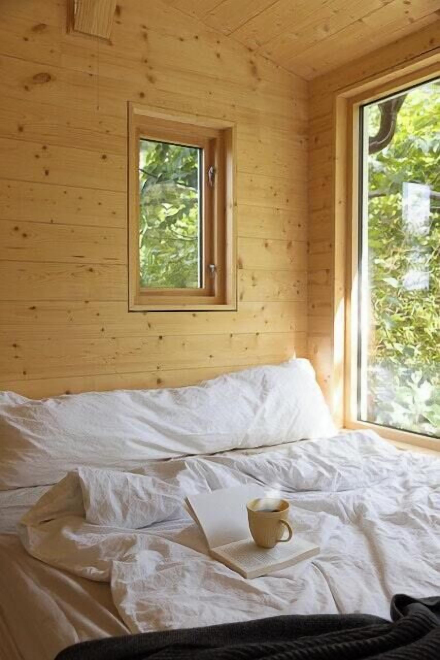 A wooden cabin room with a bed, a window, and a cup of coffee on the bed.