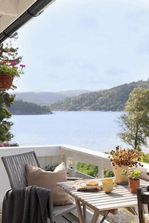 A balcony with a table and chairs, overlooking a lake and hills.