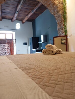Ein Zimmer mit einem Bett, einer Holzbalkendecke, einem Fernseher und einem an der Wand befestigten Regal.