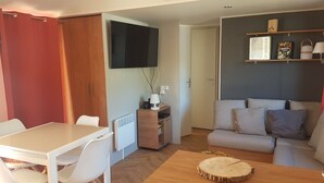 Un espacio habitable compacto con una mesa de comedor, un sofá, un televisor montado en la pared y un mueble pequeño con una lámpara.
