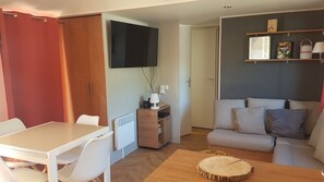 Ein gemütlicher Wohnbereich mit Esstisch, einer Couch, einem an der Wand befestigten Fernseher und einer kleinen Kommode mit Lampe.
