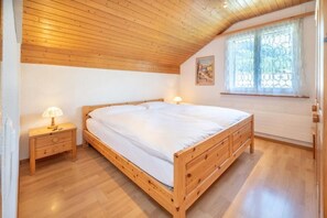 A bedroom with a wooden bed, bedside tables, and a window with a view. - Haus Cervin - Inspiringplaces Zermatt (Zermatt)