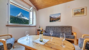 A cozy room with a wooden table, two chairs, a sofa, and a window with a mountain view. - Haus Cervin - Inspiringplaces Zermatt (Zermatt)