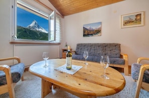 A cozy room with a wooden table, two chairs, a sofa, and a window with a mountain view. - Haus Cervin - Inspiringplaces Zermatt (Zermatt)