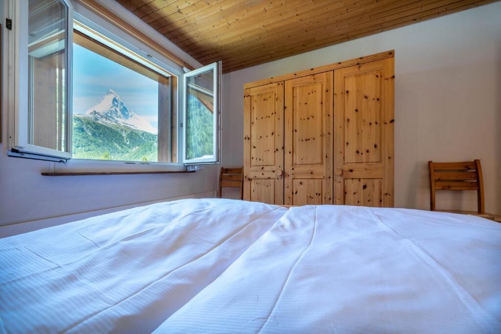 Ein Schlafzimmer mit einem großen Bett, einem Holzschrank und einem Fenster mit Blick auf die Berge.