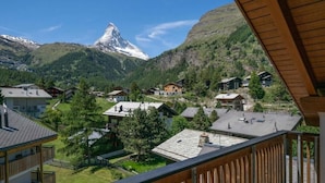 A mountain village with traditional houses, a prominent mountain peak, and a wooden balcony overlooking the village. - Haus Cervin - Inspiringplaces Zermatt (Zermatt)