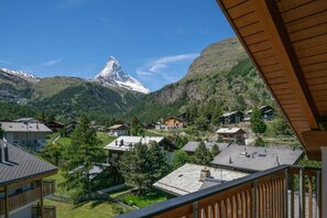 A mountain village with traditional houses, a prominent mountain peak, and a wooden balcony overlooking the village. - Haus Cervin - Inspiringplaces Zermatt (Zermatt)