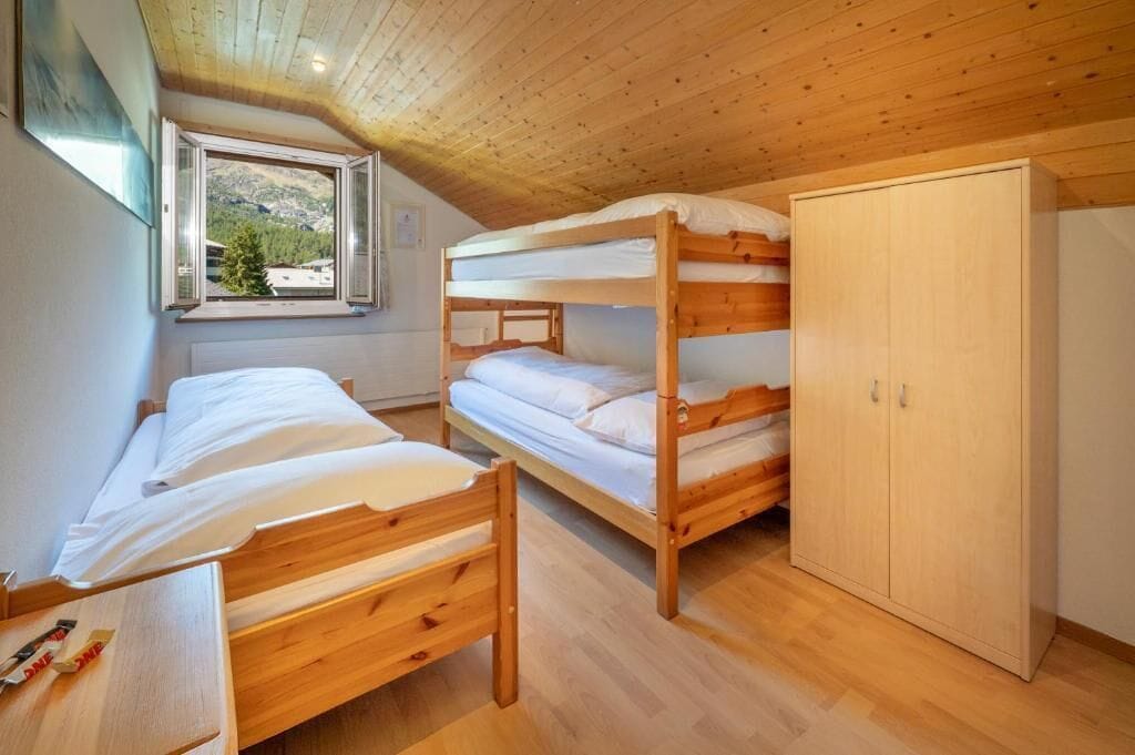 Une chambre avec des lits superposés, une armoire et une fenêtre donnant sur des arbres.