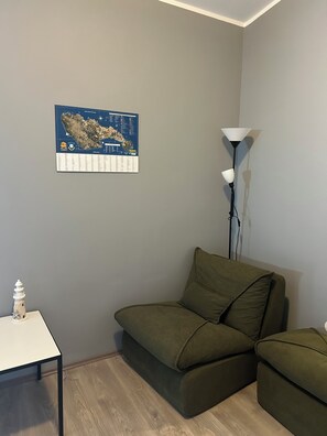 Ein Zimmer mit grauer Wand, einem grünen Sofa, einem kleinen Tisch mit einer weißen Lampe und einer Karte an der Wand.