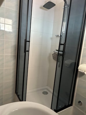 Eine gläserne Duschkabine mit gefliestem Boden in Weiß und einer weißen Badewanne im Vordergrund.