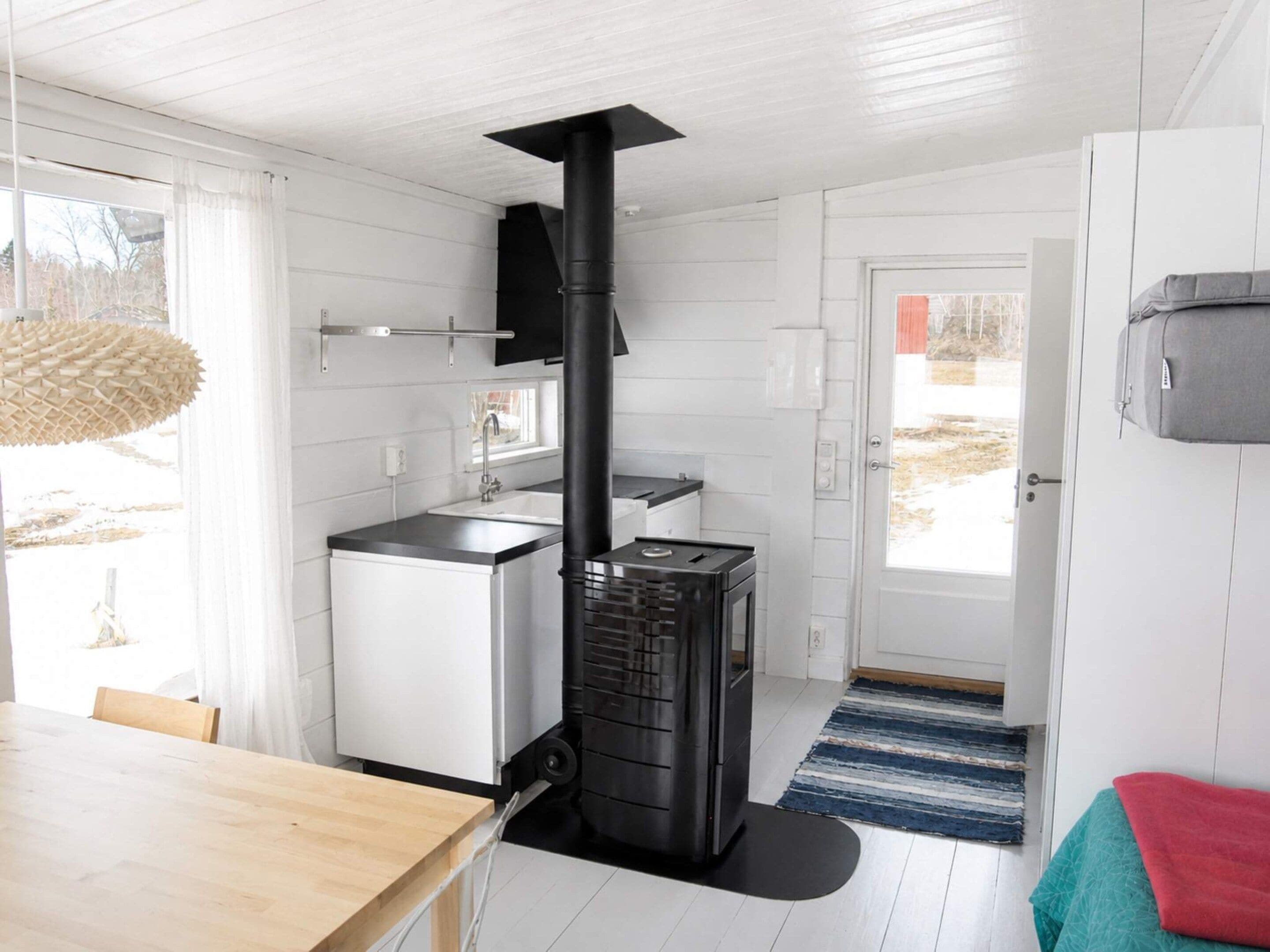 A modern kitchen with a wood-burning stove, white cabinetry, and a dining area with a wooden table.