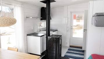 A modern kitchen with a wood-burning stove, white cabinetry, and a dining area with a wooden table.