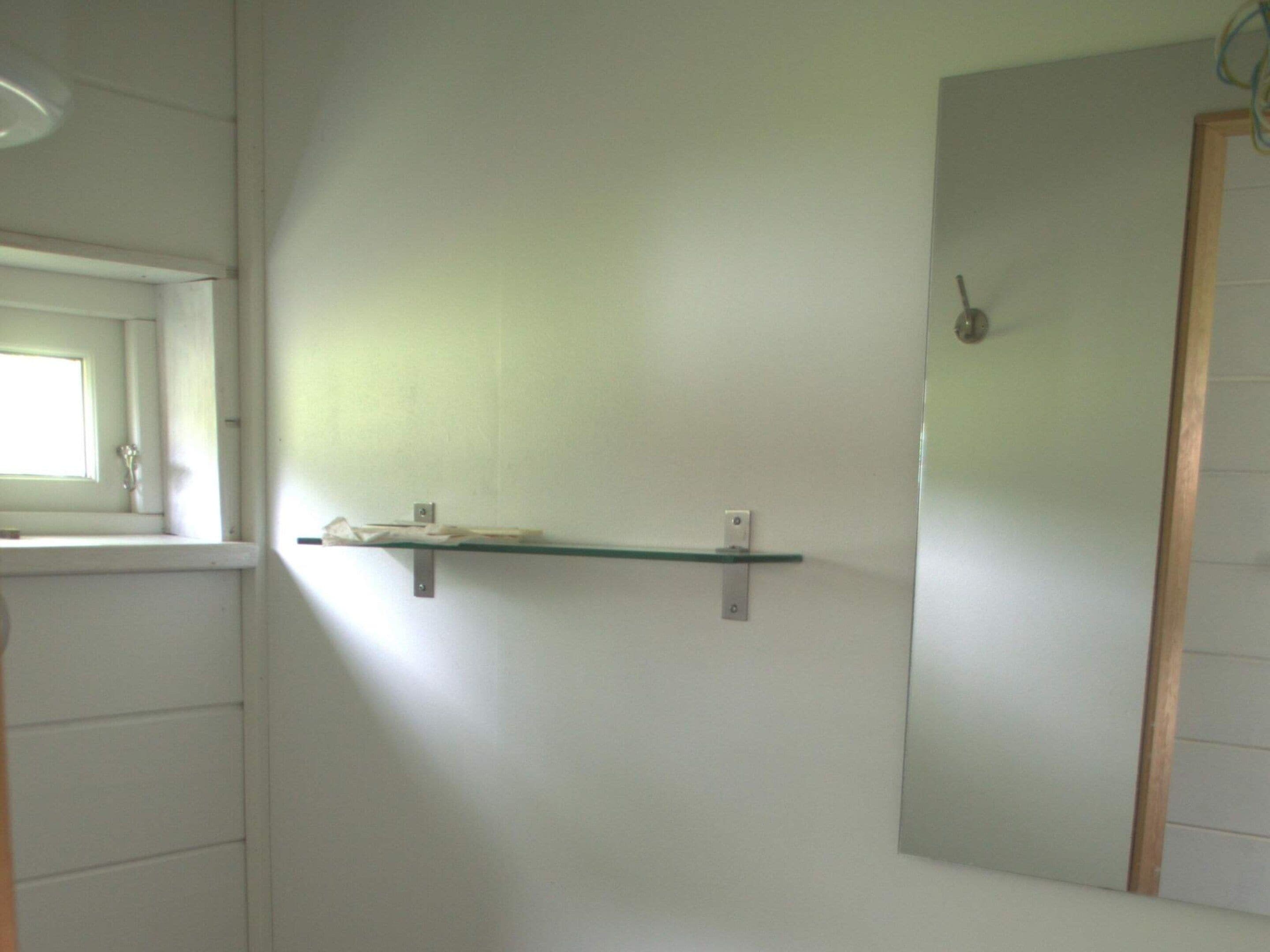 A bathroom with a mirror, a shelf, and a window.